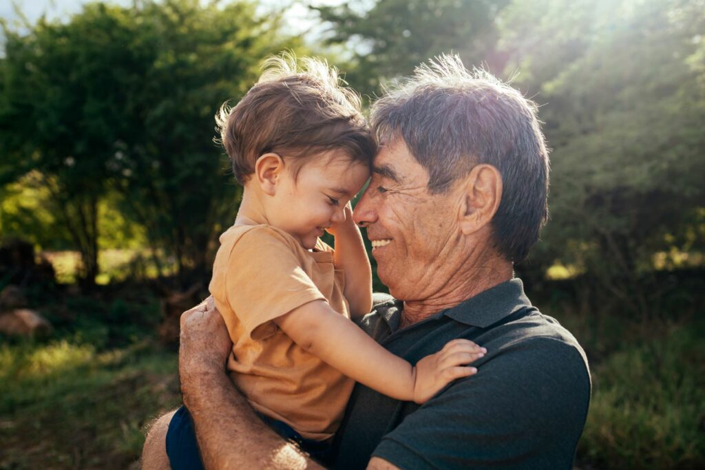 Grandfather and young child smiling forehead-to-forehead outdoors
