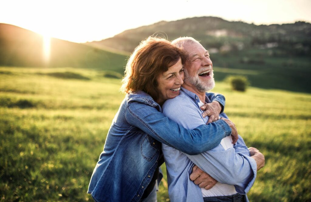 Laughing older couple embracing in a sunlit green field