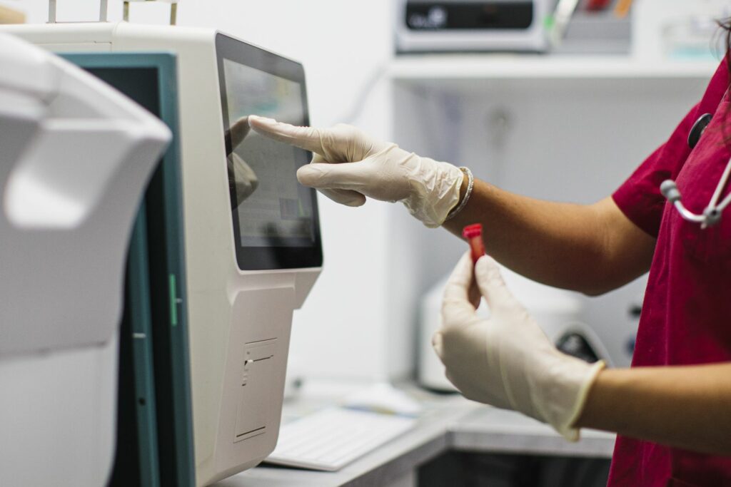 Gloved healthcare worker operates lab analyzer with sample vial