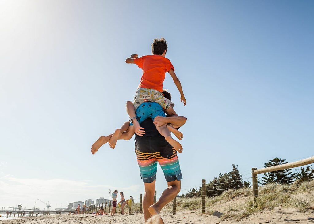 Adult carrying two children on shoulders at beach