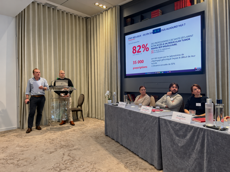 Presenters address healthcare panel beside oncology statistics screen